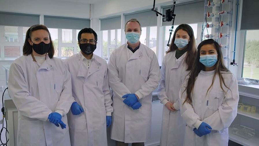 Mahmood Mirza and 4 colleagues in the lab in white coats and masks.